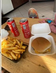 Cheeseburger met friet en een blikje cola op een houten tafel