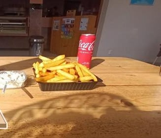 Bakje verse friet met een blikje cola op een zonnige tafel