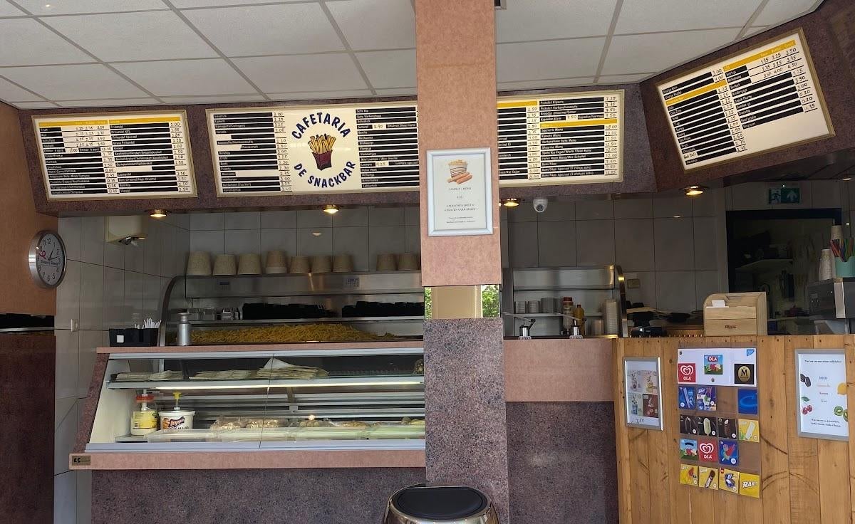 Het interieur van Cafetaria de Snackbar in Dinteloord, met de menuborden boven de toonbank en verse friet in de warmhoudbak